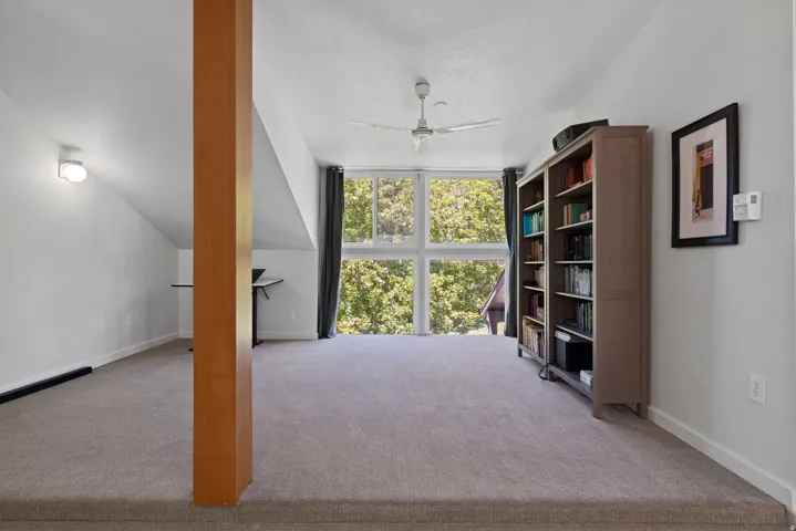 Primary bedroom area featuring a large window, sloped ceilings, and a ceiling fan