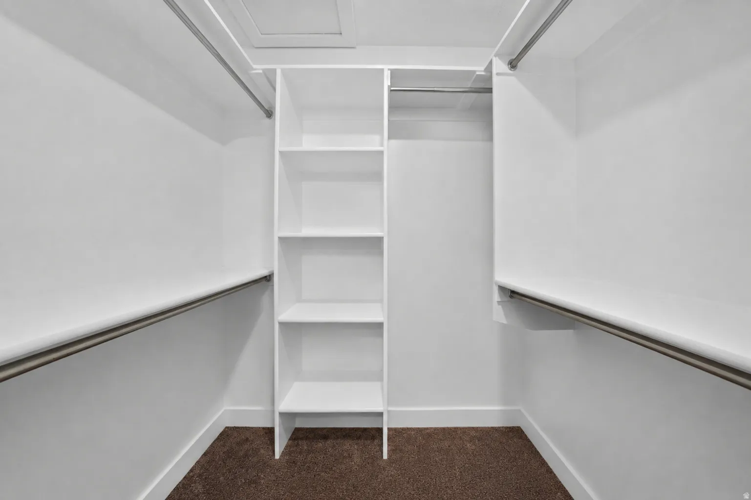 Walk-in closet featuring built-in shelving, dual hanging rods, white walls, white baseboards, and brown carpeting