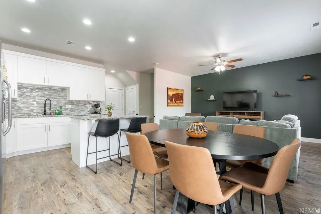 Open-concept living area featuring wood-finish flooring, a kitchen with white cabinetry, a stone-look backsplash, a kitchen island with seating, and recessed lighting