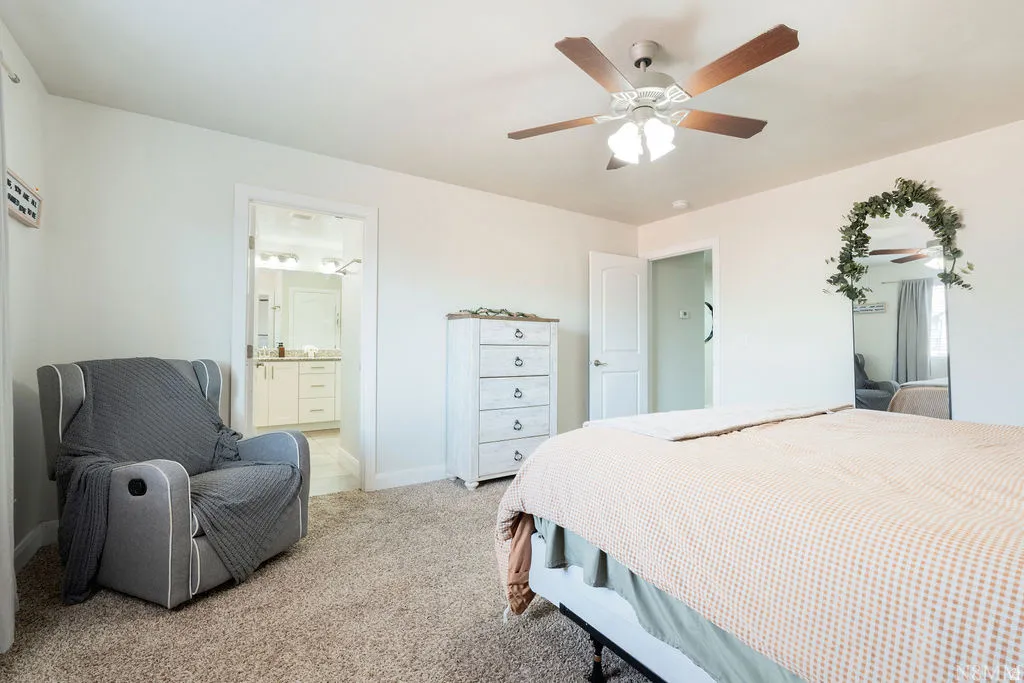 Carpeted bedroom with a ceiling fan light fixture and direct access to a bathroom