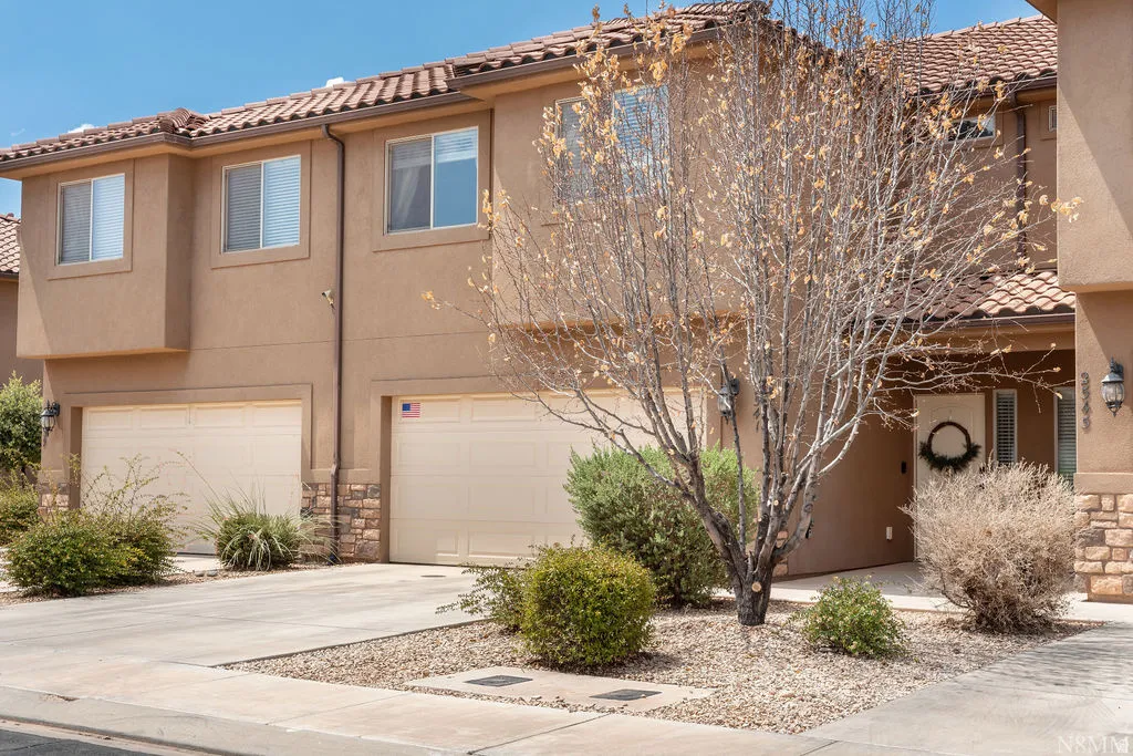 Stucco exterior featuring dual garage doors, a tile roof, and stone accents