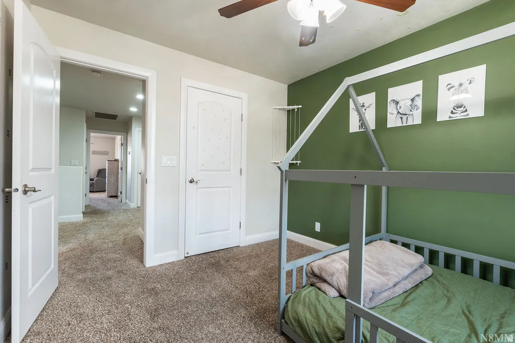 Carpeted room featuring a green accent wall with decorative wall trim and a ceiling fan