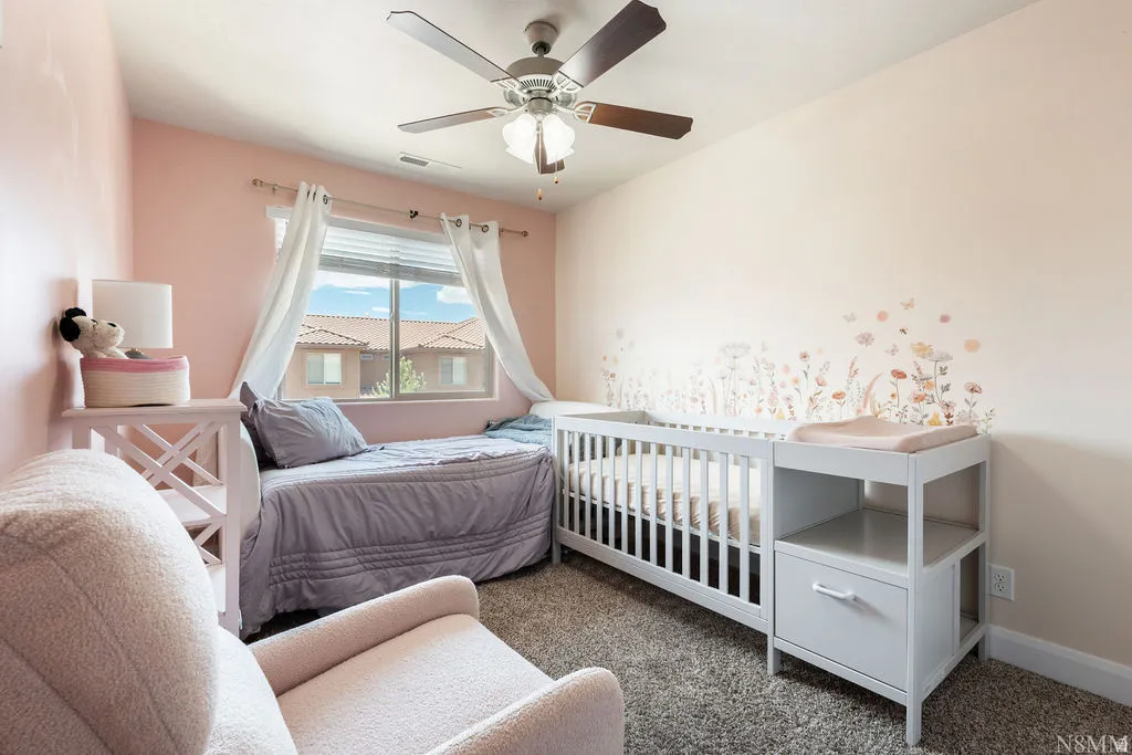 Carpeted room featuring a ceiling fan with light fixture, a window with blinds, and wall decor