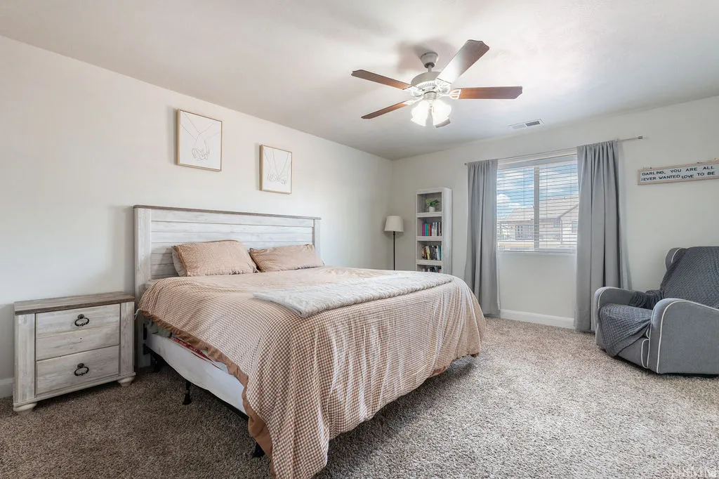 Neutral tone wall paint, textured carpeting, and a ceiling fan with light fixture