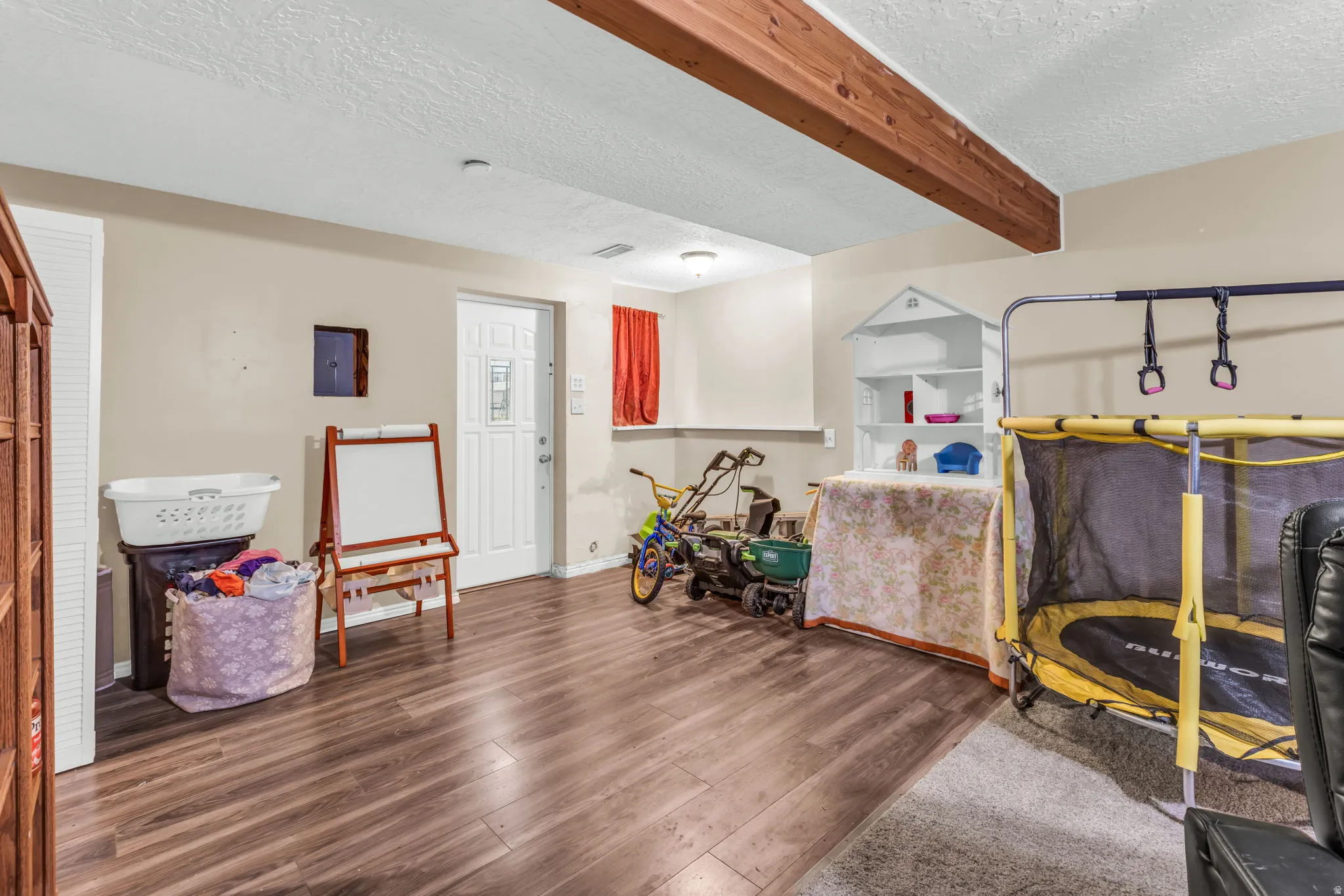 Wood-finish flooring throughout a versatile interior space featuring exposed wood beams, a white paneled door, and neutral wall tones