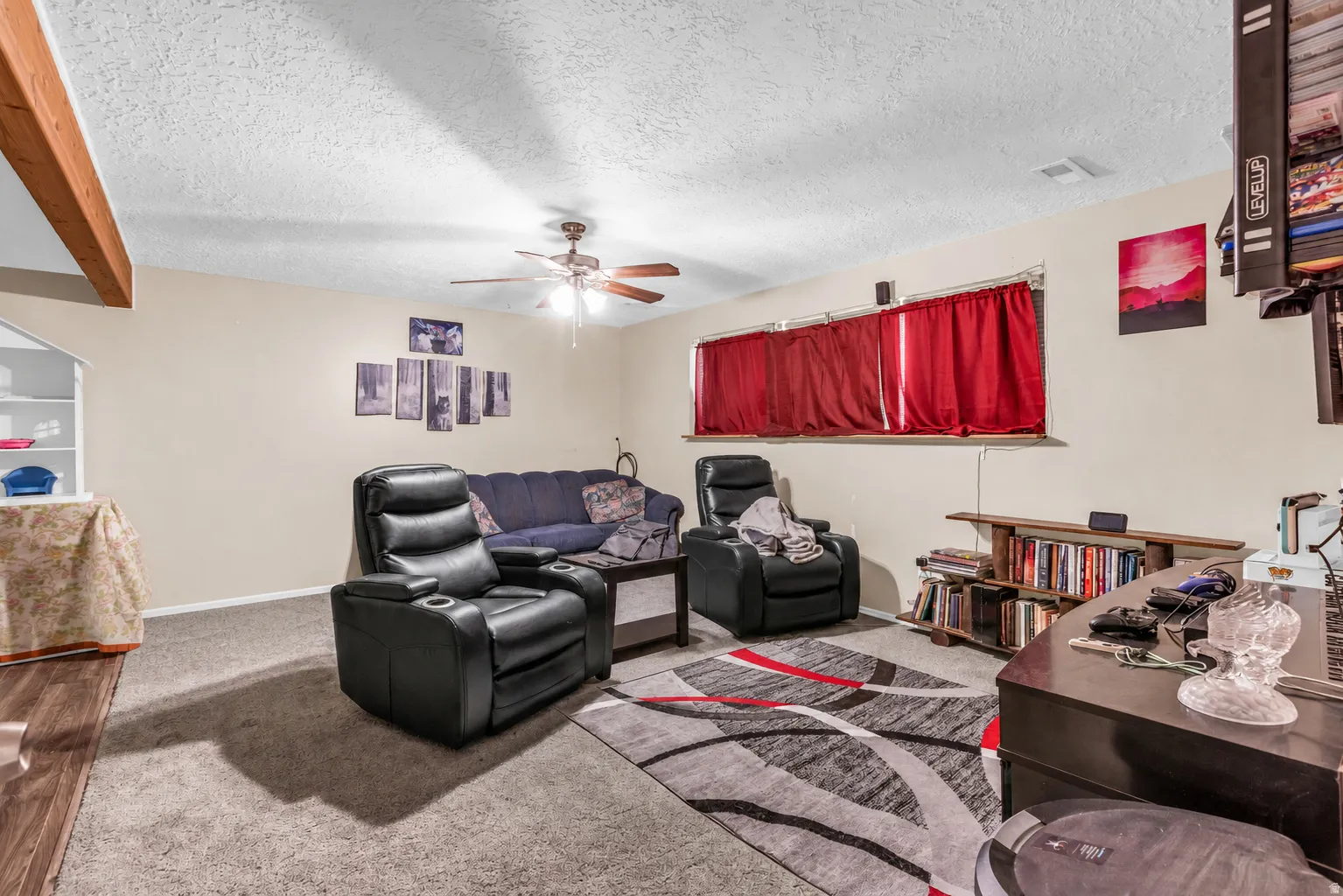 Plush carpeting, wood-finish flooring, wood beam accent, built-in shelving, and a ceiling fan with light fixture
