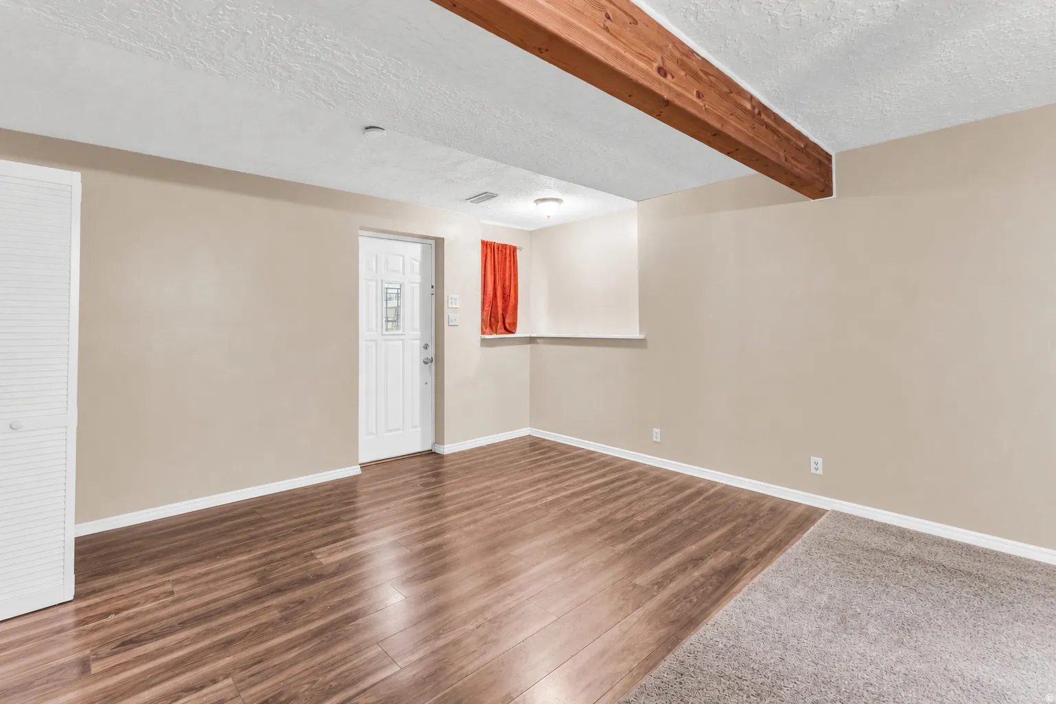 Wood-finish flooring, exposed wood beam, white paneled door, and built-in closet with louvered doors