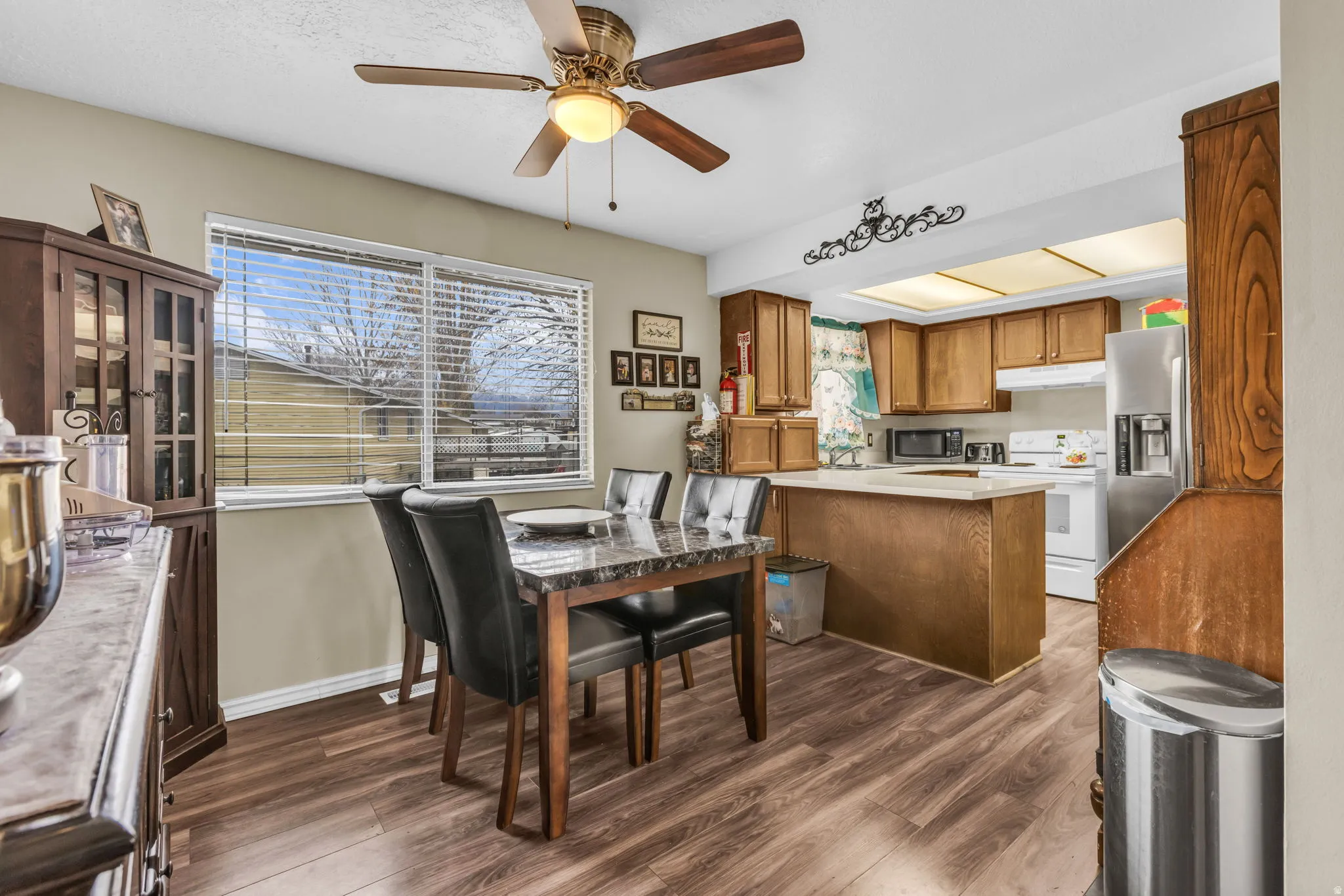 Dining area featuring wood-finish flooring, a contemporary dining set with a marble-look table and black upholstered chairs, and a large window with blinds