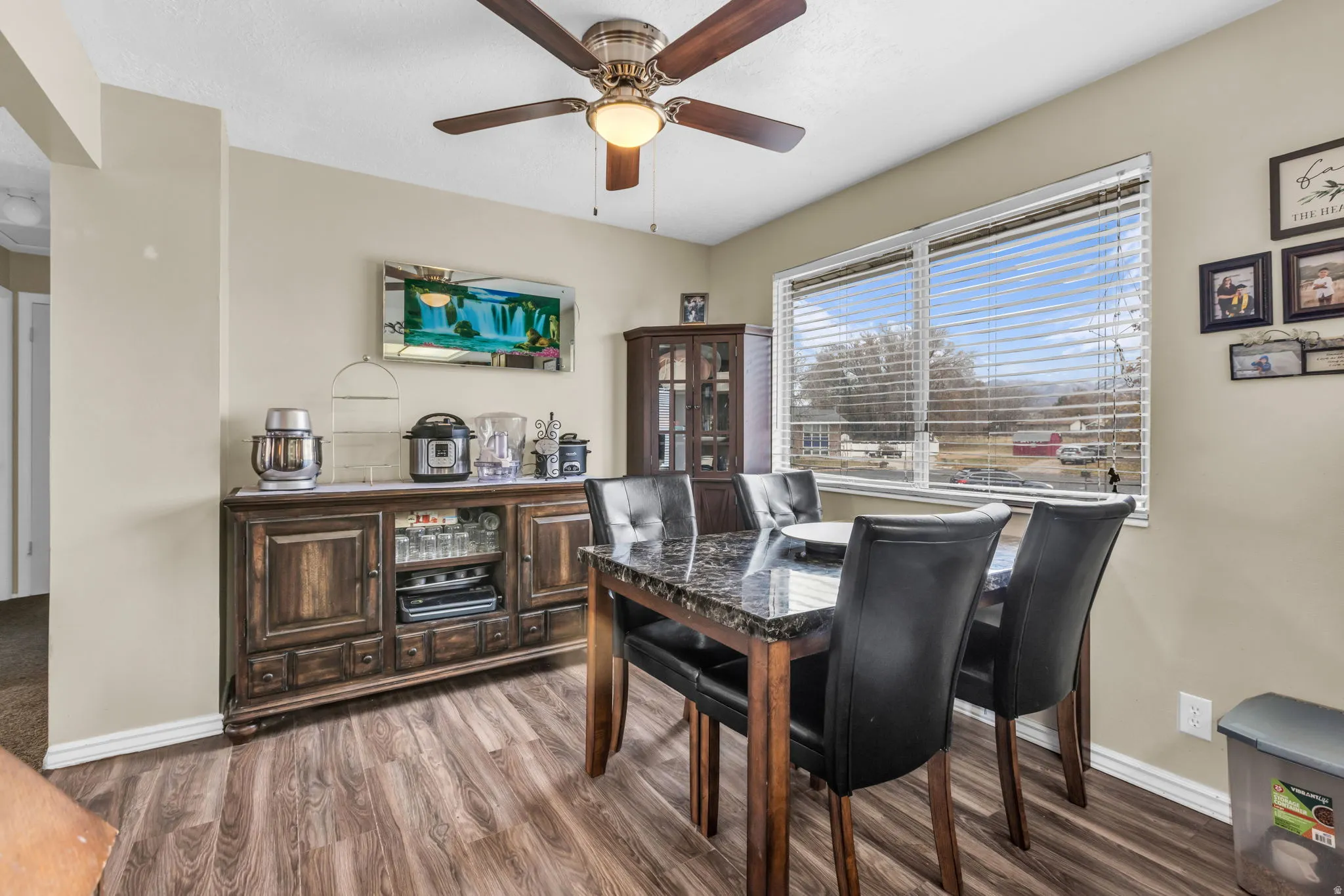 Dining area featuring wood-finish flooring, a ceiling fan with integrated lighting, and a large window with horizontal blinds