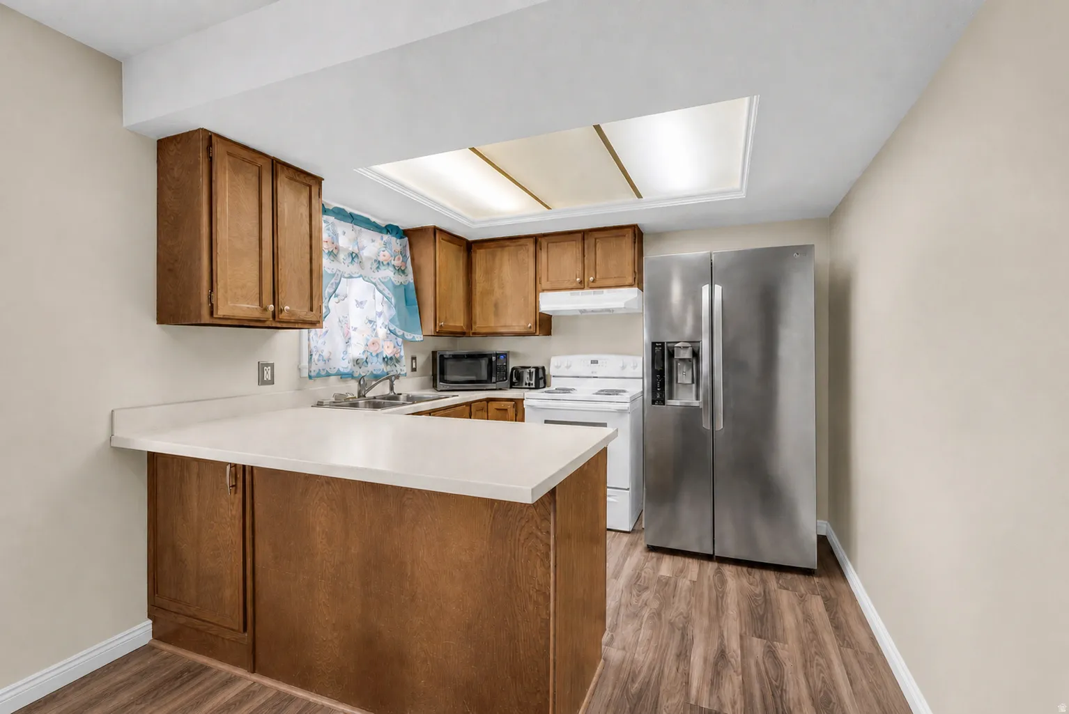 Kitchen featuring wood-finish cabinetry, light-toned countertops, stainless steel refrigerator, white electric range, and wood-finish flooring