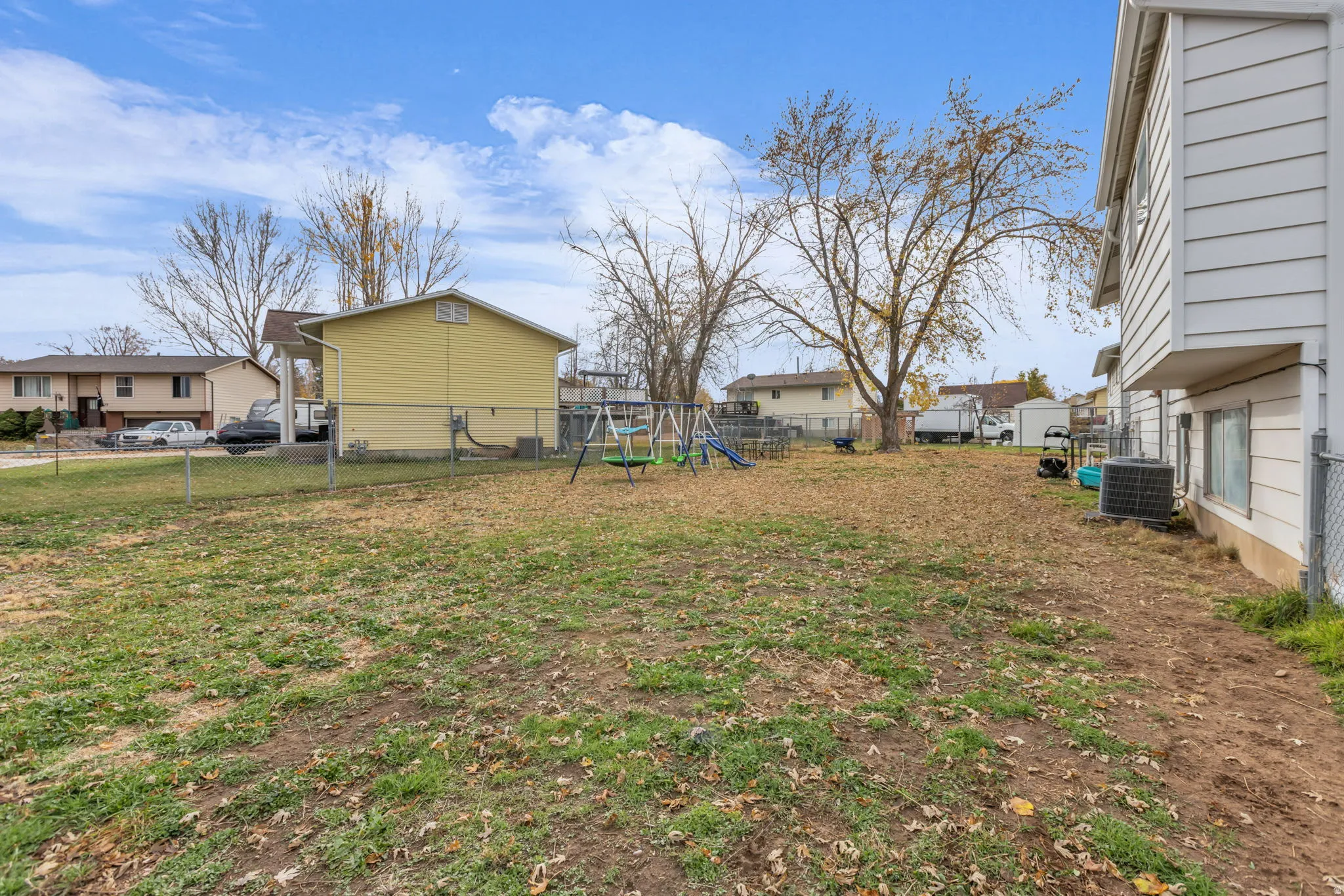 Spacious fenced backyard featuring a large open lawn area, mature trees, and a chain-link perimeter fence