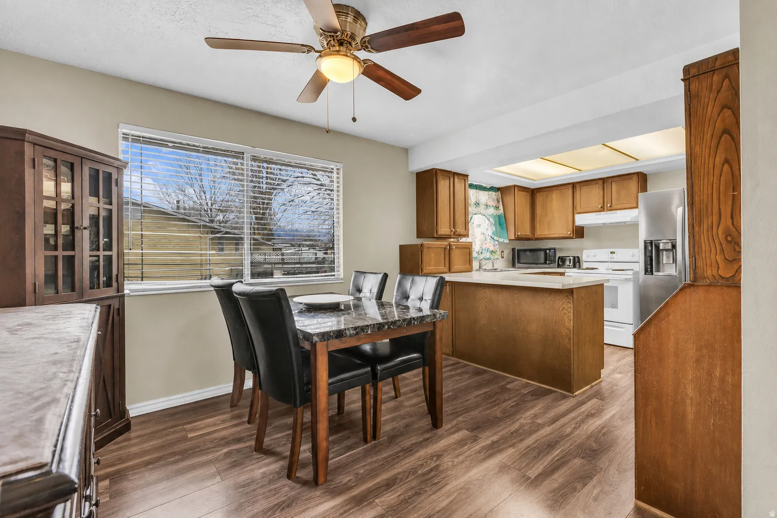 Wood-finish flooring throughout, featuring a kitchen with wood cabinetry and white appliances, a kitchen island with a light-toned countertop, and a dining area with a window