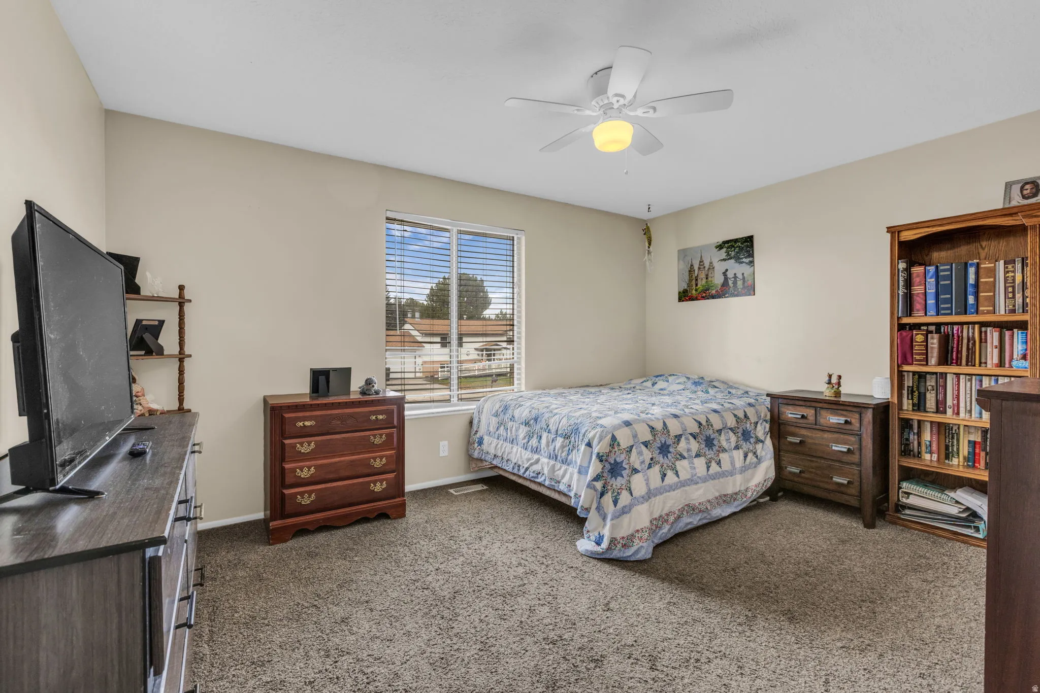 Carpeted interior room featuring light-toned walls, a ceiling fan with integrated lighting, and a window with horizontal blinds