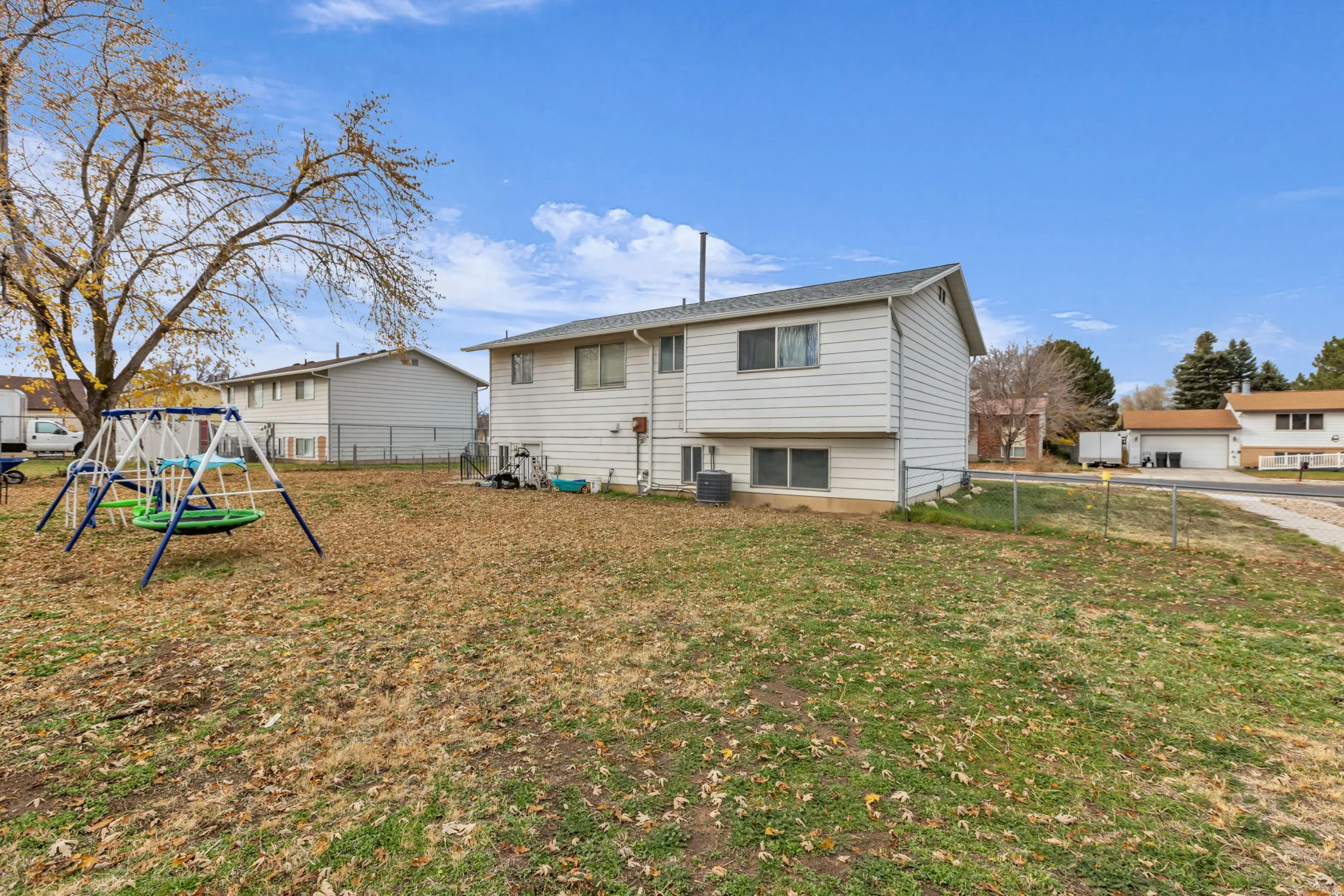 Spacious backyard featuring a chain-link fence, mature tree, and a two-story residence with white siding