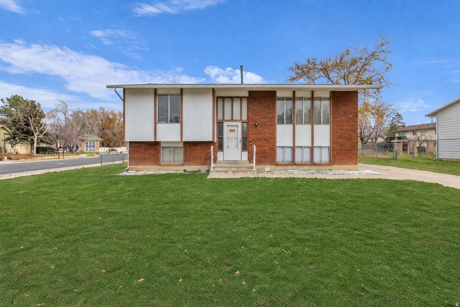 Split-level exterior featuring brick and vertical siding, a front entry with a storm door, and a spacious front lawn