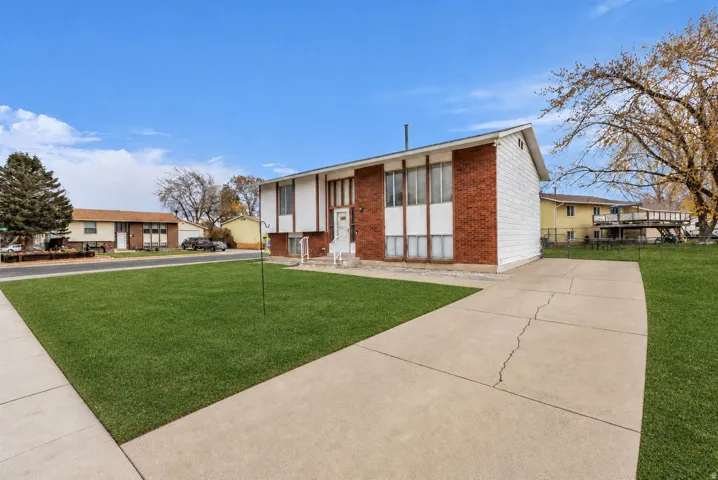 Split-level exterior with brick and siding facade, concrete driveway, front lawn, and mature trees