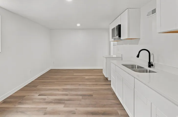 Modern kitchen area featuring white cabinetry, light-toned countertops, and a double basin stainless steel sink with a matte black faucet