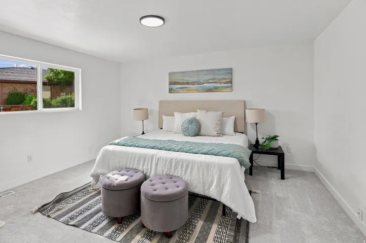 Bright bedroom featuring light gray carpeting, white walls, a large window, and a flush-mount ceiling light fixture