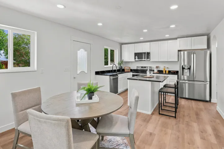 Open-concept kitchen featuring white cabinetry, black countertops, stainless steel appliances, and a central island with seating