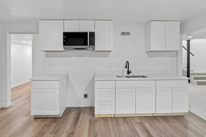 Modern kitchen area featuring white shaker-style cabinetry, light-toned countertops, a stainless steel undermount sink with a matte black faucet, and an over-the-range microwave