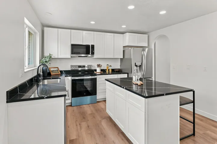 Bright kitchen featuring white cabinetry, dark countertops, stainless steel appliances, an arched doorway, and wood-finish flooring