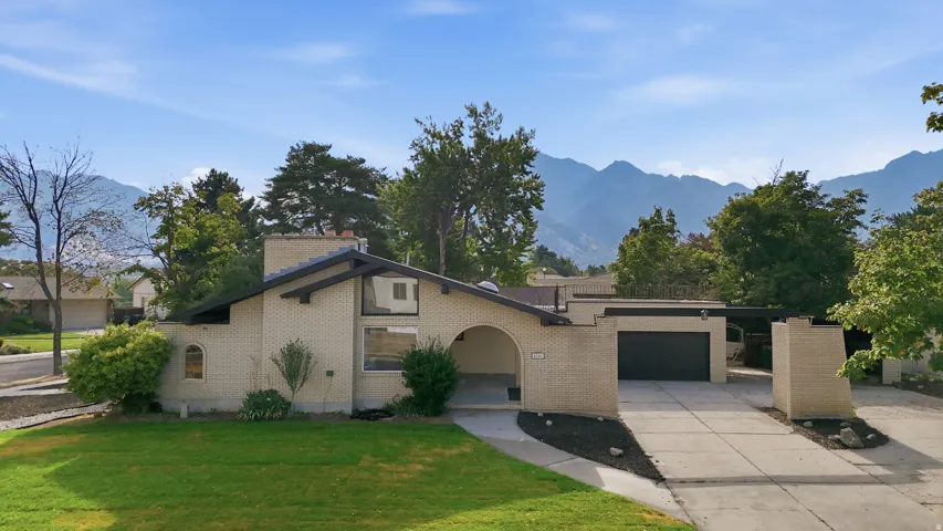 Mid-century modern residence featuring light-colored brick exterior, a prominent chimney, and a dark asphalt shingle roof