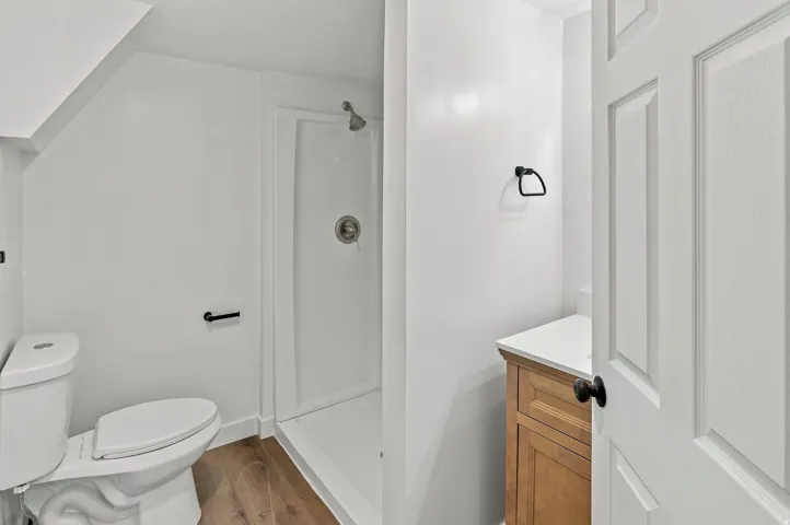 Full bathroom featuring a white toilet, enclosed shower with a white pan and surround, and wood-finish flooring
