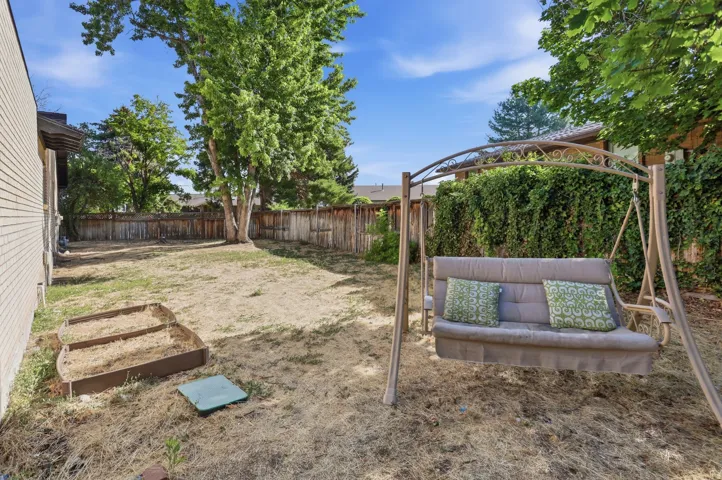 Spacious backyard featuring a privacy fence, mature trees, and a brick exterior