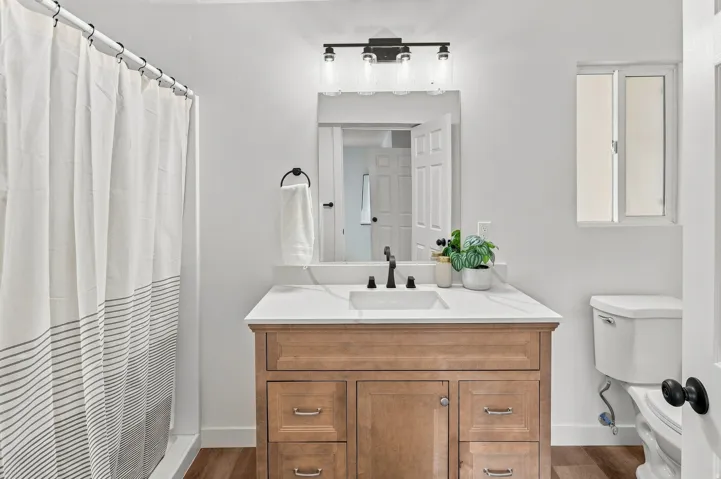 Bathroom featuring a wood-finish vanity with a white countertop and integrated sink, matte black faucet, and rectangular mirror