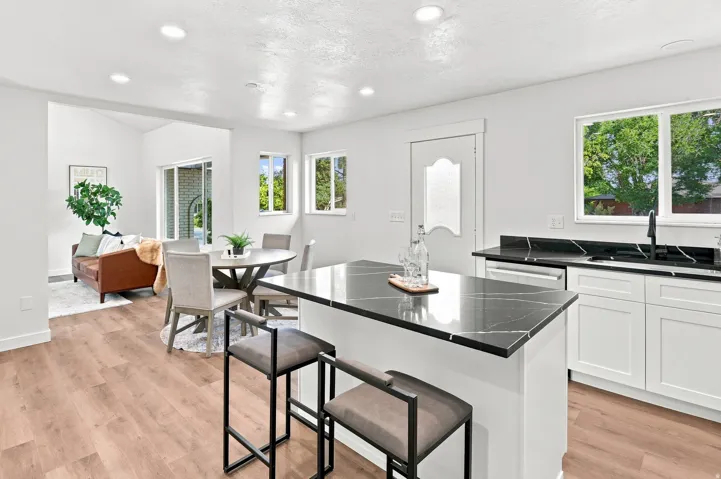 Open-concept kitchen and dining area featuring wood-finish flooring, white cabinetry, and black countertops with white veining