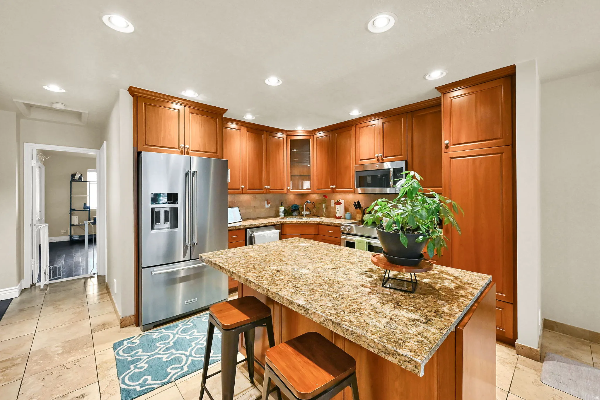 Kitchen featuring a central island with a granite-style countertop, recessed lighting, wood cabinetry, stainless steel appliances, and tile flooring
