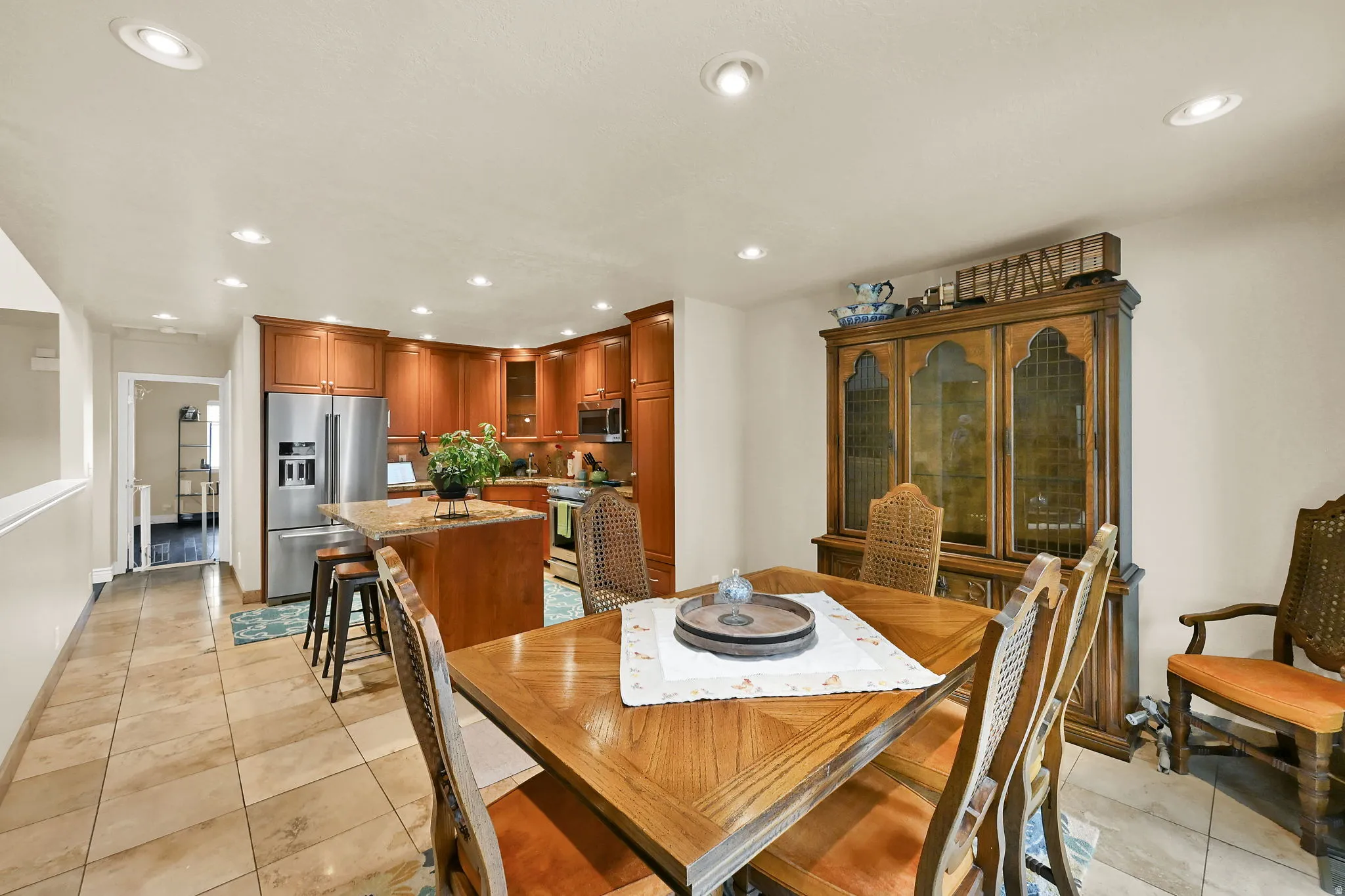 Kitchen and dining area featuring recessed lighting, a stainless steel refrigerator, wood cabinetry, a center island with bar seating, and tile flooring