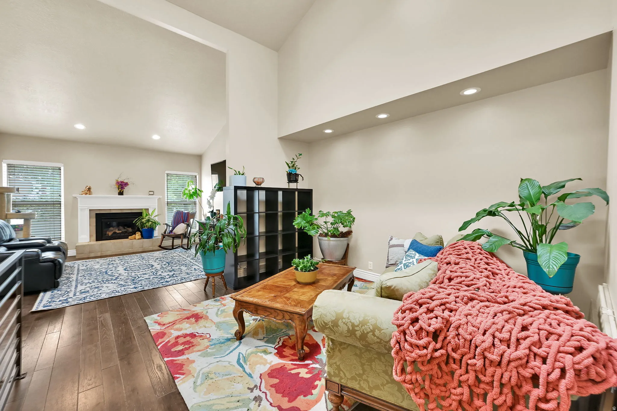 Spacious living area featuring vaulted ceilings, wood-finish flooring, recessed lighting, and a fireplace with a white mantel and tiled hearth