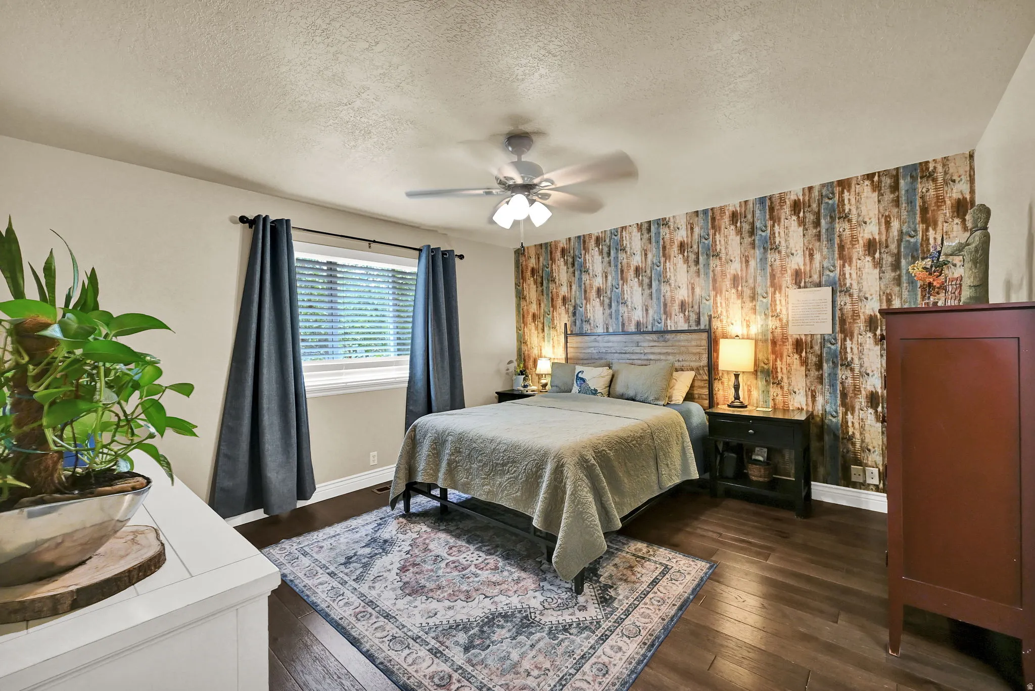Bedroom featuring wood-finish flooring, a textured accent wall, and a ceiling fan with integrated lighting