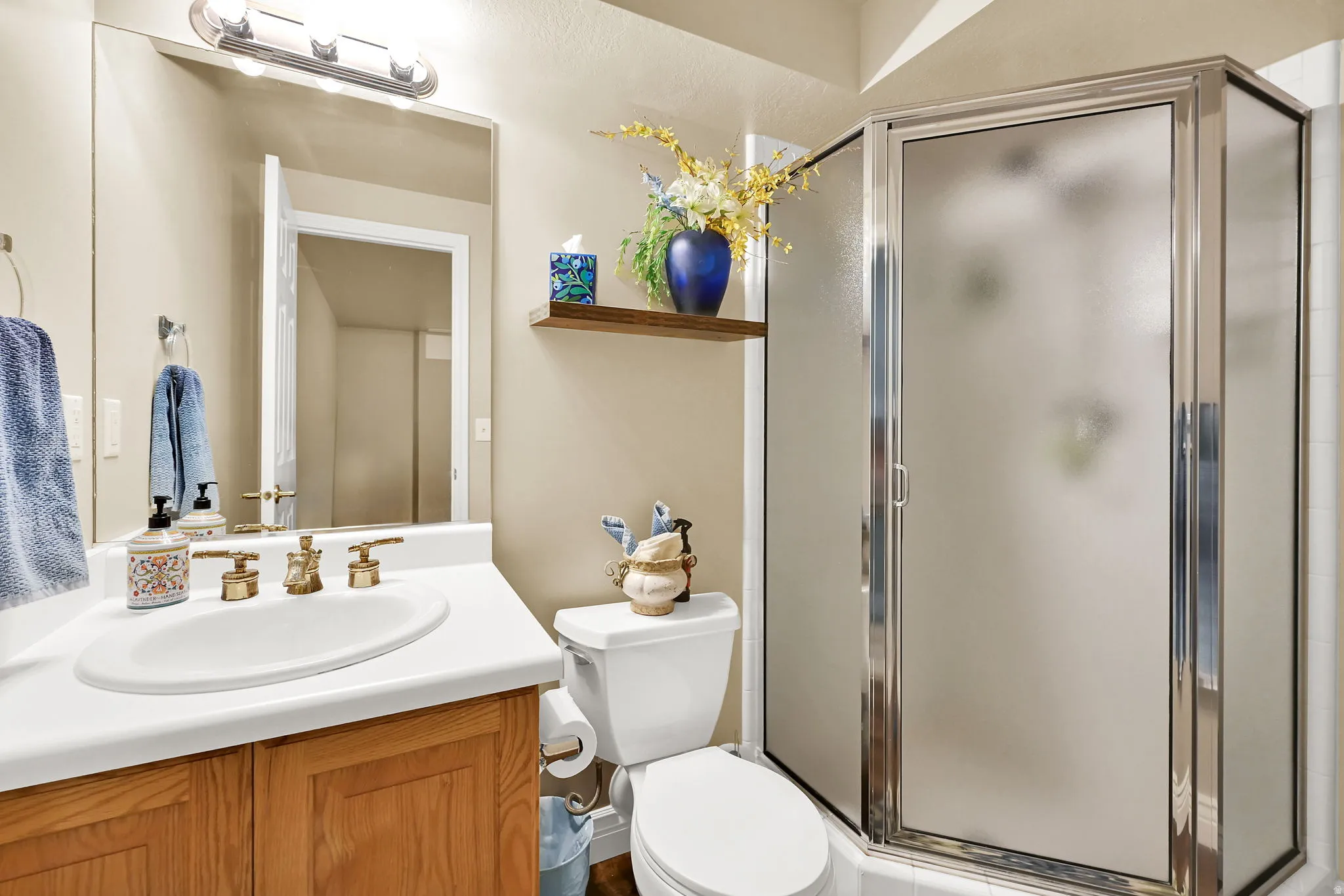 Bathroom featuring a corner shower with frosted glass enclosure, a vanity with wood-finish cabinetry, a white countertop with an integrated sink, and a large wall-mounted mirror