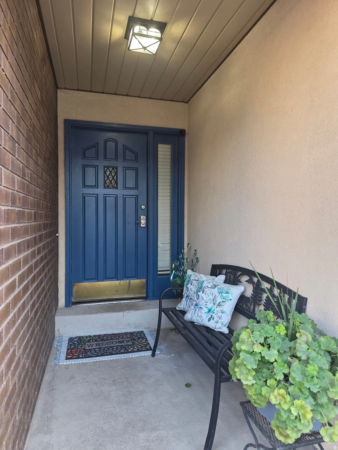 Entryway featuring a paneled blue front door with a side light, brick exterior wall, stucco finish, concrete porch, and a ceiling-mounted light fixture