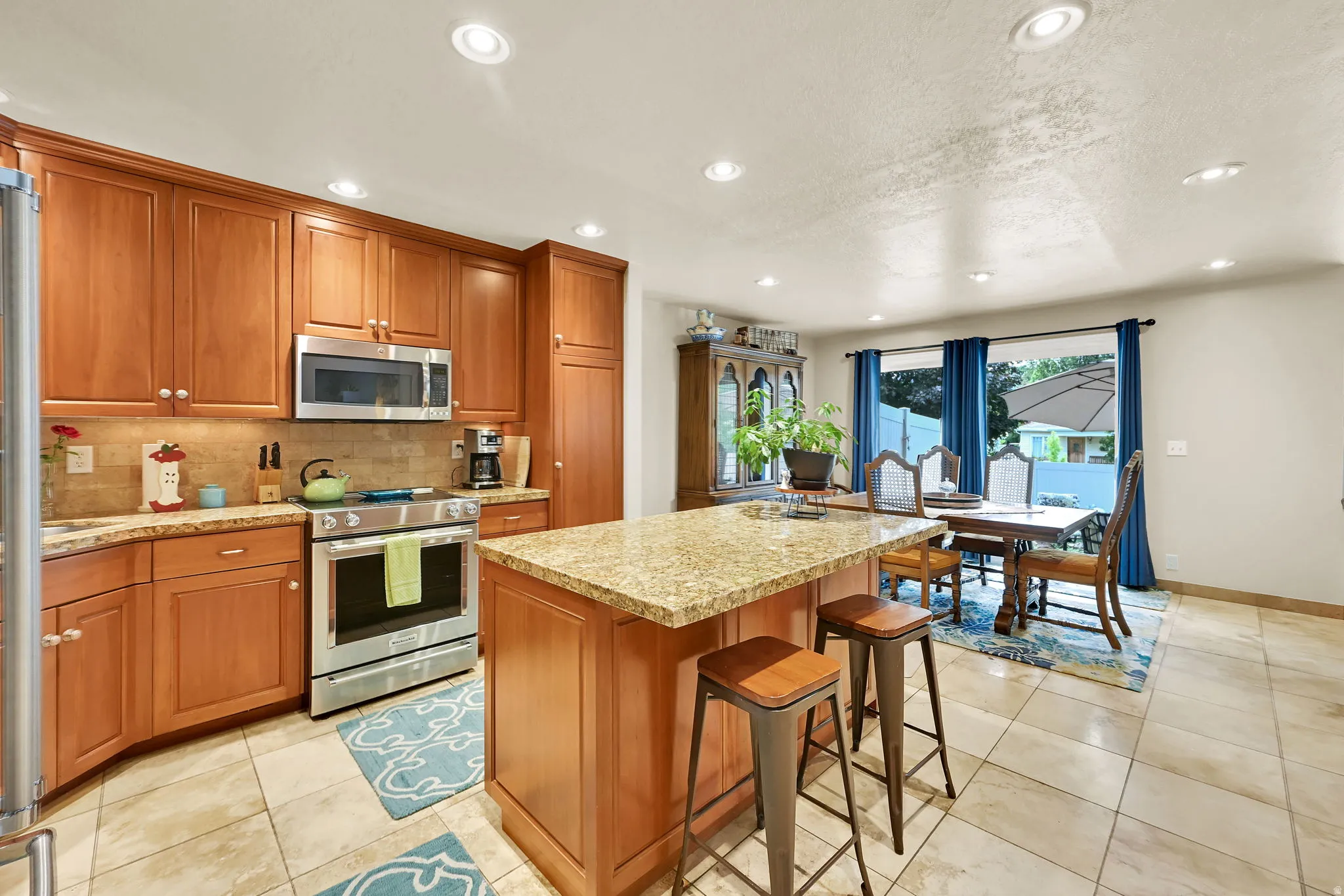 Kitchen featuring abundant wood cabinetry, stainless steel appliances including a microwave and range, light-toned stone countertops, and a coordinating stone tile backsplash