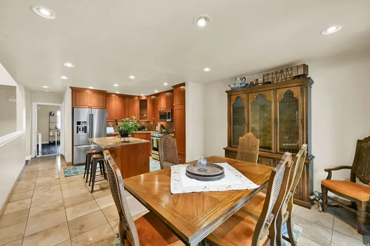 Kitchen and dining area featuring recessed lighting, a stainless steel refrigerator, wood cabinetry, a center island with bar seating, and tile flooring