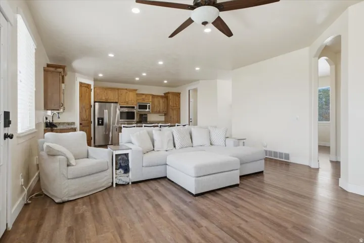 Open-concept living area with wood-finish flooring, a ceiling fan, recessed lighting, and a kitchen featuring wood cabinetry and stainless steel appliances
