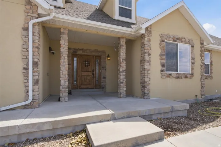 Stucco exterior featuring stone veneer accents around windows and on structural columns, a double wood-finish entry door with decorative ironwork, and a concrete front porch