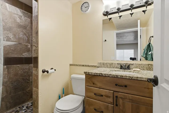 Bathroom featuring a stone-tiled shower with a pebble floor, a wood-finish vanity with a light-colored countertop, and a vanity mirror with an attached light fixture