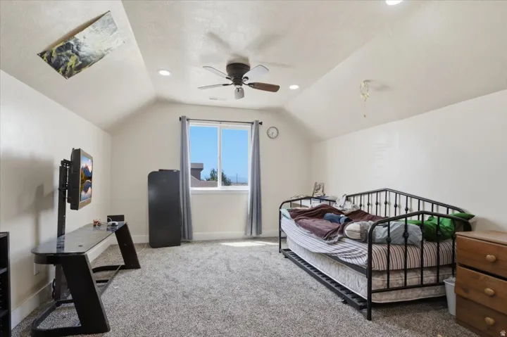 Spacious room featuring vaulted ceilings, recessed lighting, a ceiling fan, a window with natural light, and grey carpet flooring