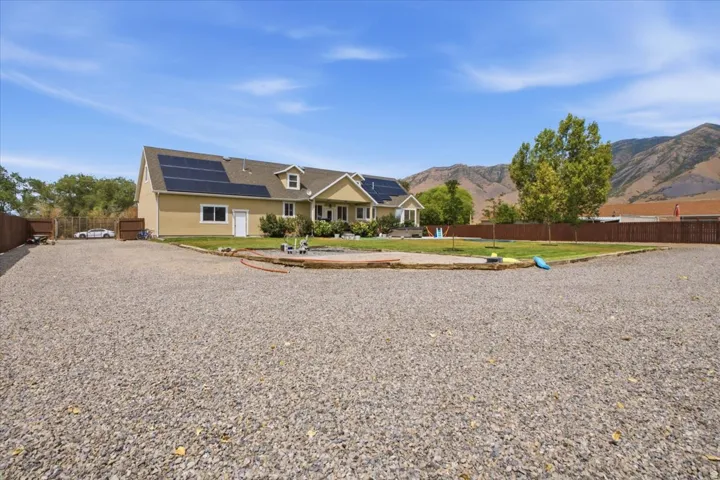 Spacious gravel driveway with a large residential structure featuring solar panels, dormer windows, and a covered entry