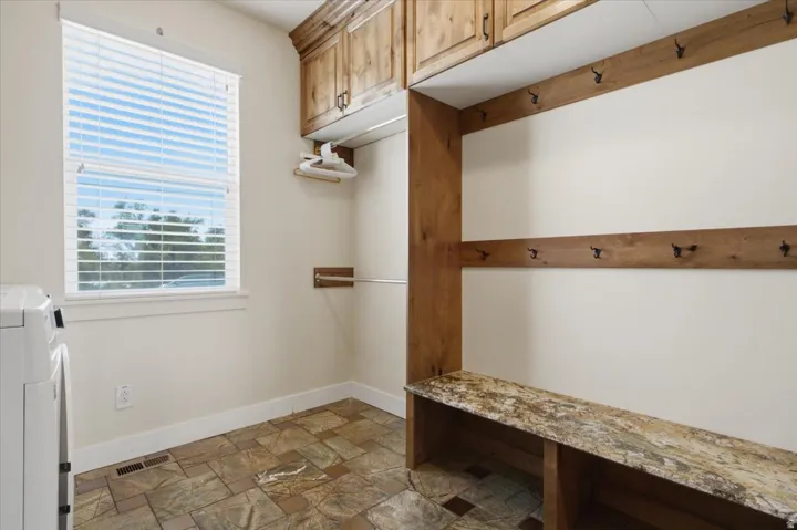 Utility room featuring wood-finish cabinetry, a built-in bench with a stone-finish surface, and integrated coat hooks