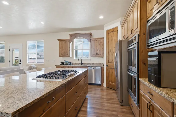 Kitchen featuring wood cabinetry, stainless steel appliances, a center island with an integrated gas cooktop, stone countertops, and wood-finish flooring