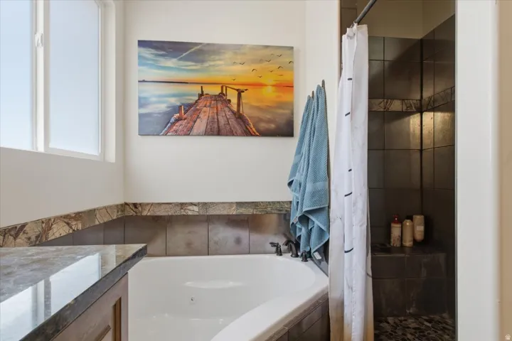 Corner soaking tub with dark stone surround, adjacent to a shower enclosure featuring dark tile walls and a built-in bench