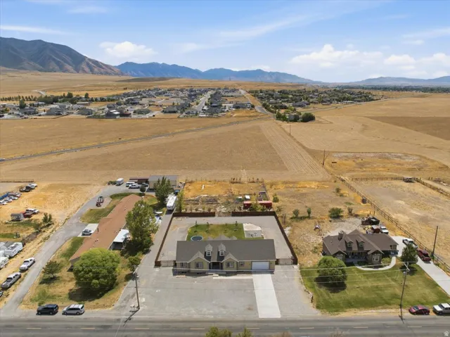 Aerial view showcasing a residential property with a multi-car driveway, fenced backyard, and surrounding open fields