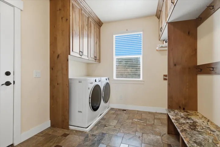 Laundry room featuring wood cabinetry, a built-in bench with a stone-look top, and slate-style floor tiling