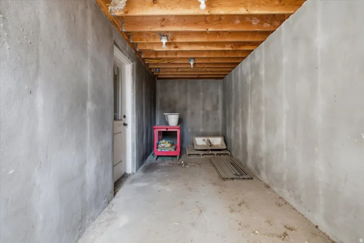 Unfinished basement space featuring exposed wood joists and concrete walls