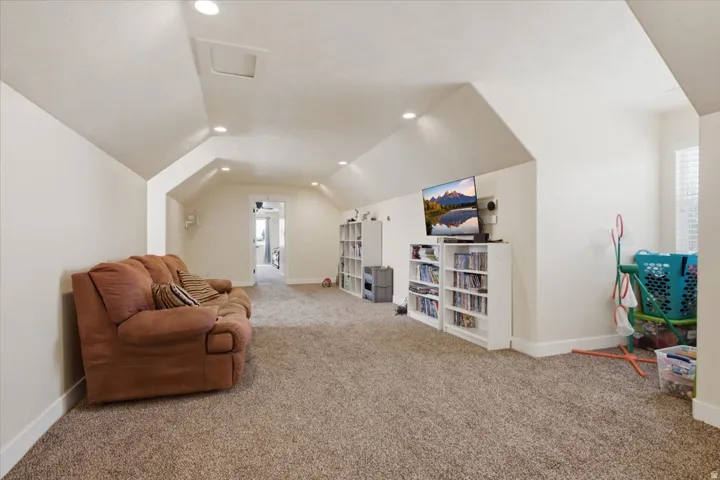 Spacious bonus room featuring vaulted ceilings, recessed lighting, neutral carpeting, and a doorway opening to another room